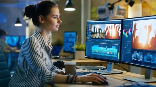 Woman sitted in front of a computer with two monitors editing videos